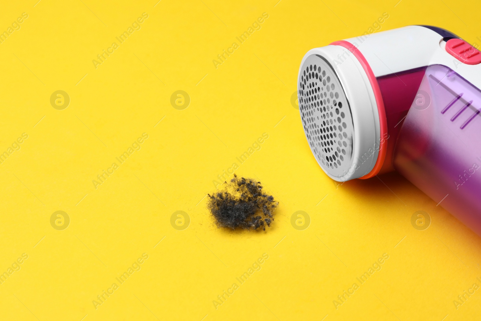 Photo of Modern fabric shaver and lint on yellow background, closeup. Space for text