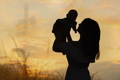 Mother with baby walking outdoors at sunset, silhouette