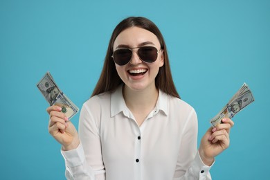 Happy woman with dollar banknotes on light blue background