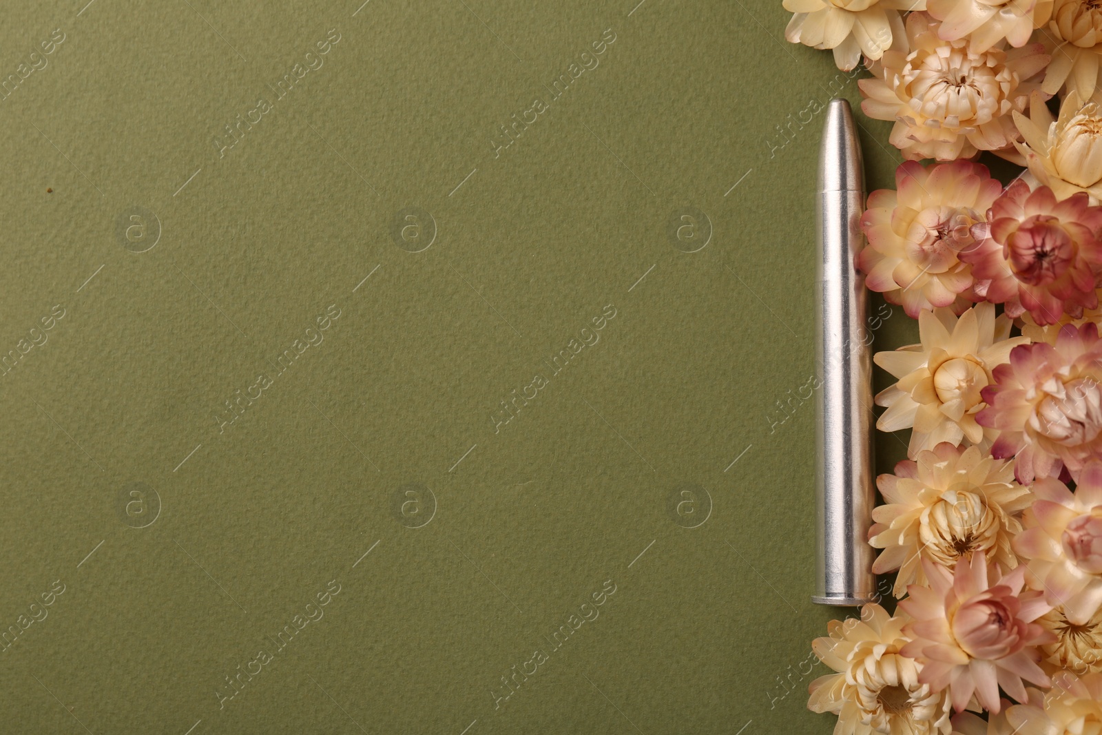 Photo of One bullet and beautiful flowers on green background, flat lay. Space for text