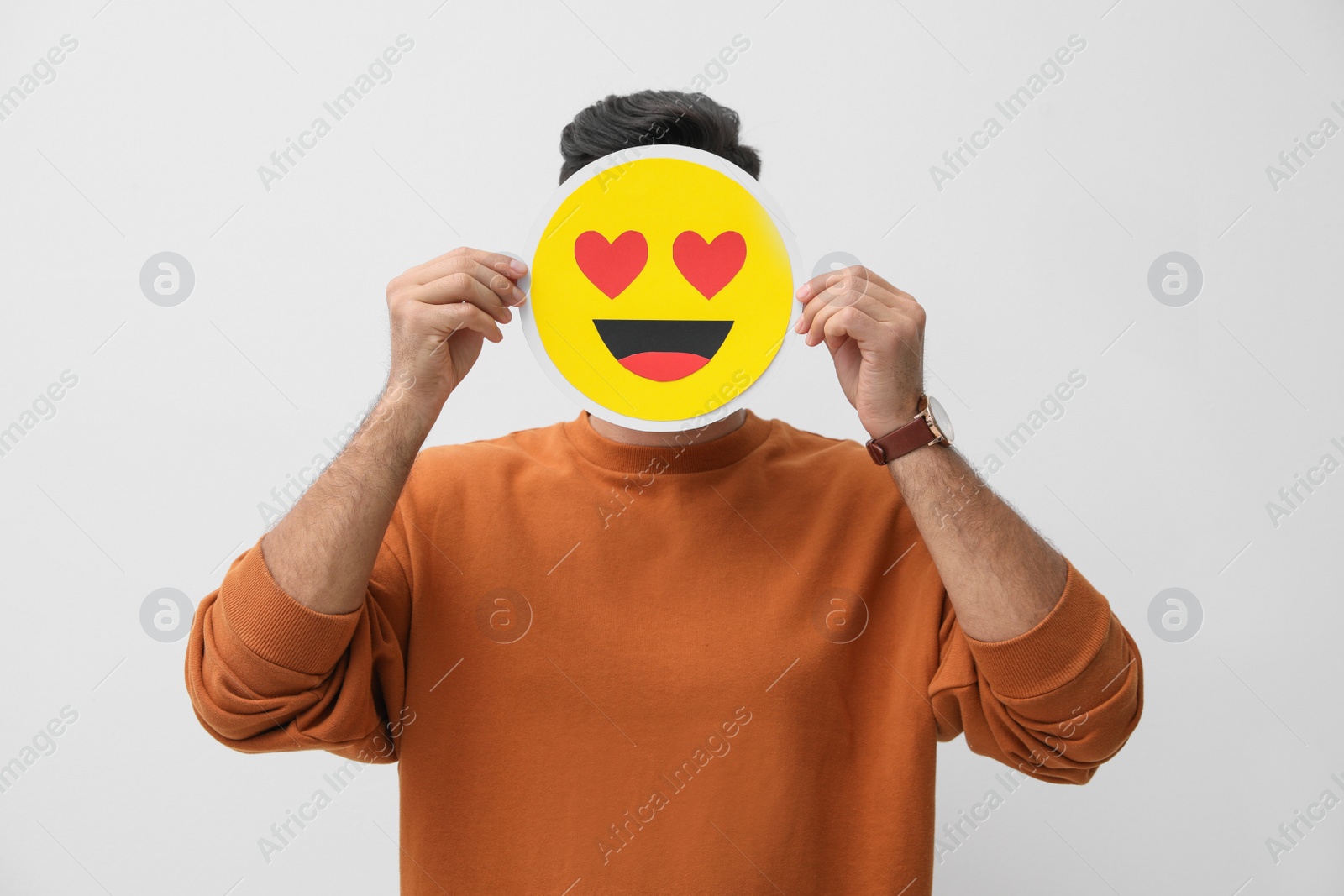 Photo of Man hiding emotions using card with drawn smiling face on white background