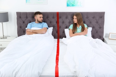 Upset couple with relationship problems lying separately in bed at home