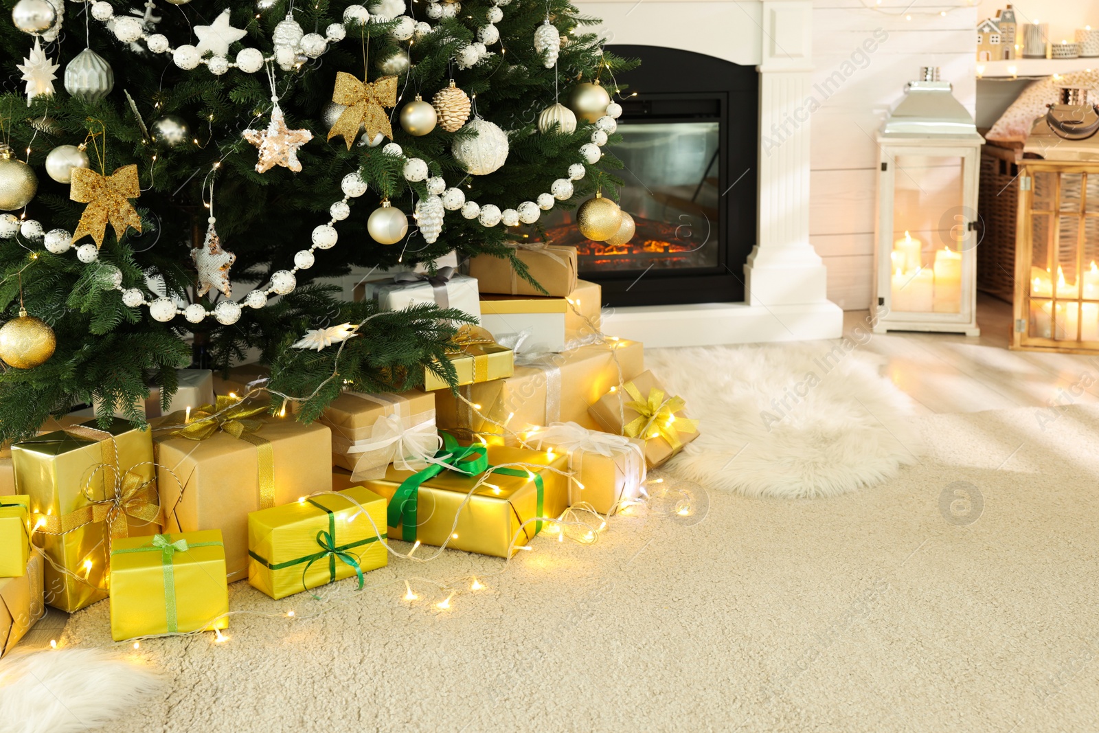 Photo of Decorated Christmas tree with gift boxes and fireplace in room