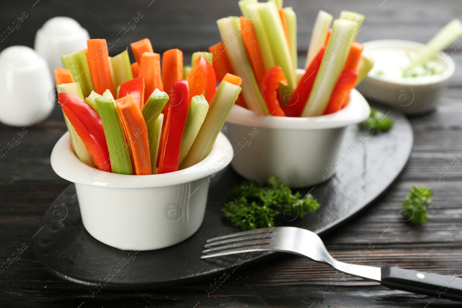 Photo of Celery and other vegetable sticks in bowls on dark wooden table