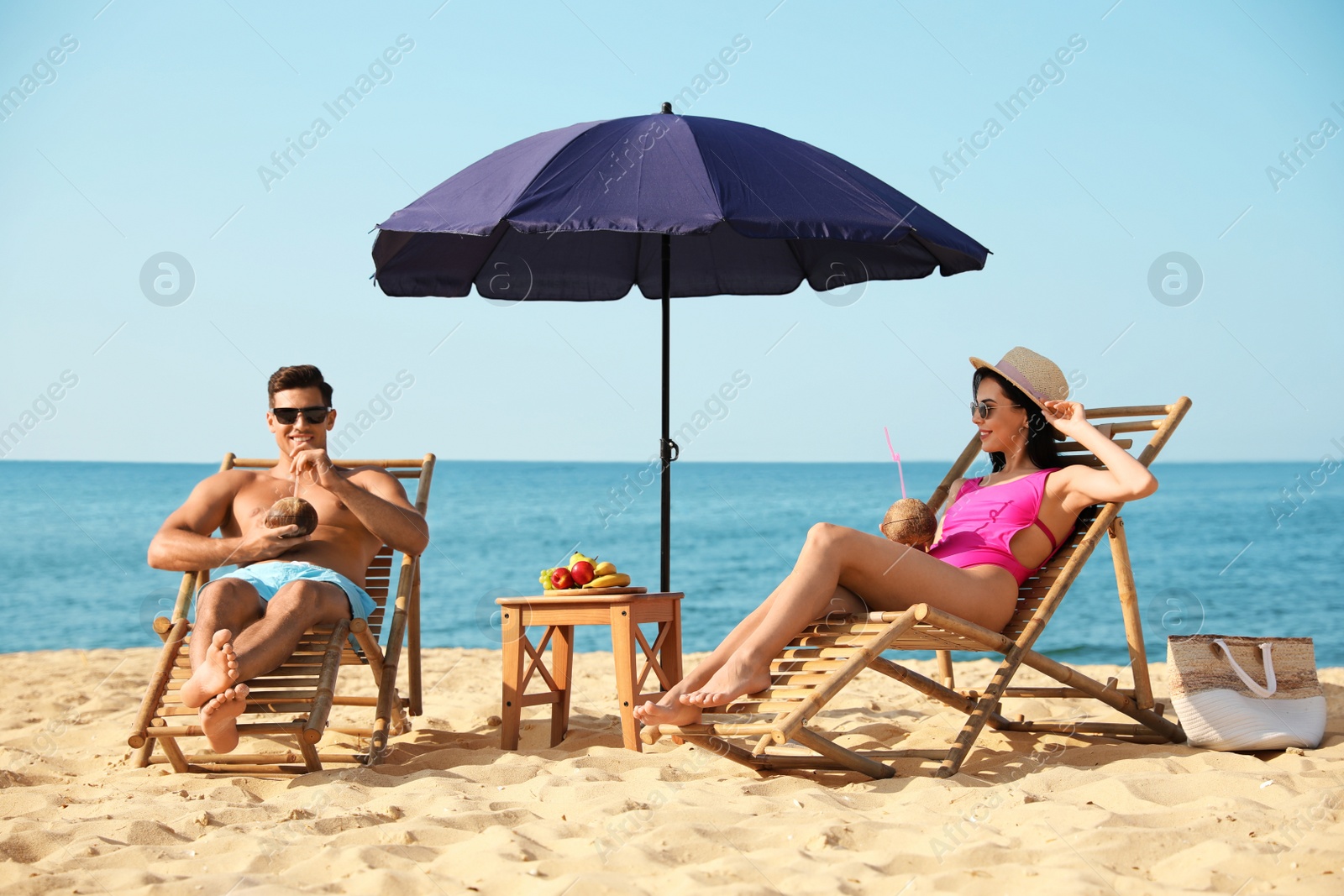 Photo of Couple with drinks resting on sunny beach at resort