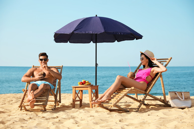 Couple with drinks resting on sunny beach at resort