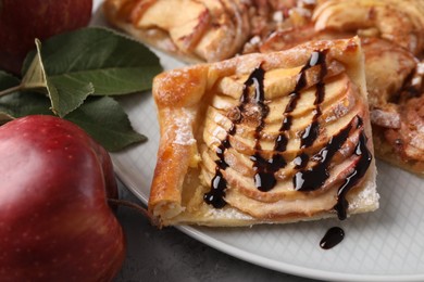 Piece of tasty apple pie with chocolate topping, fresh fruits and green leaves on table, closeup