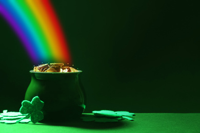 Pot with gold coins and clover leaves on green table, space for text. St. Patrick's Day celebration