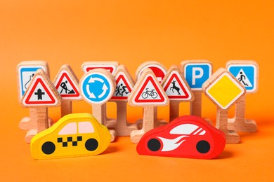 Photo of Set of wooden road signs and cars on orange background. Children's toy