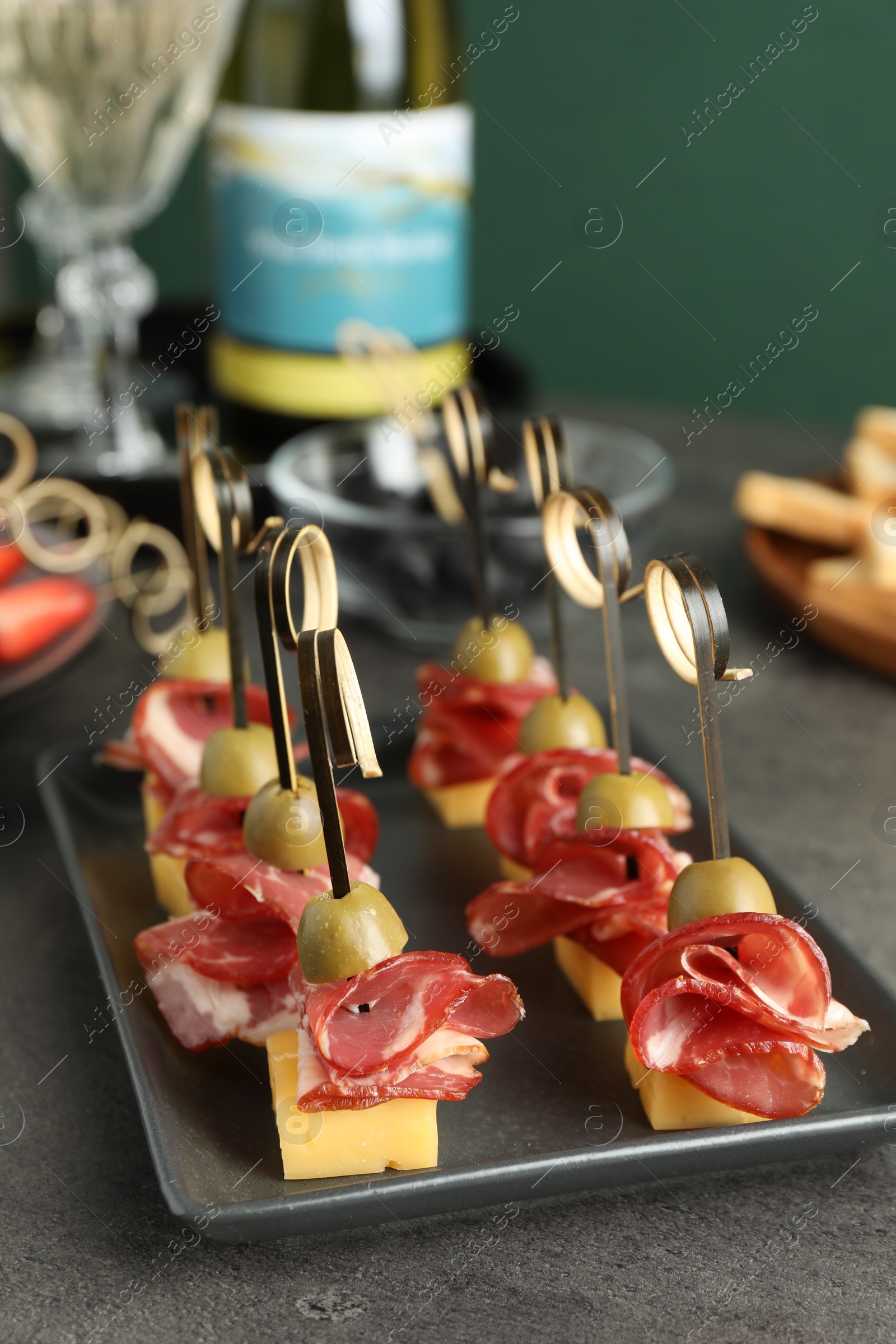 Photo of Tasty canapes with olives, prosciutto and cheese on grey table, closeup