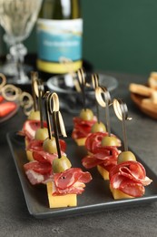 Tasty canapes with olives, prosciutto and cheese on grey table, closeup