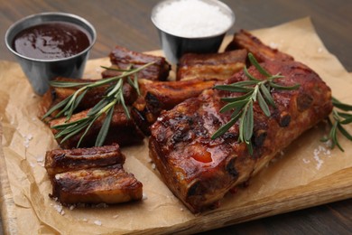 Photo of Tasty roasted pork ribs served with sauce and rosemary on wooden table, closeup