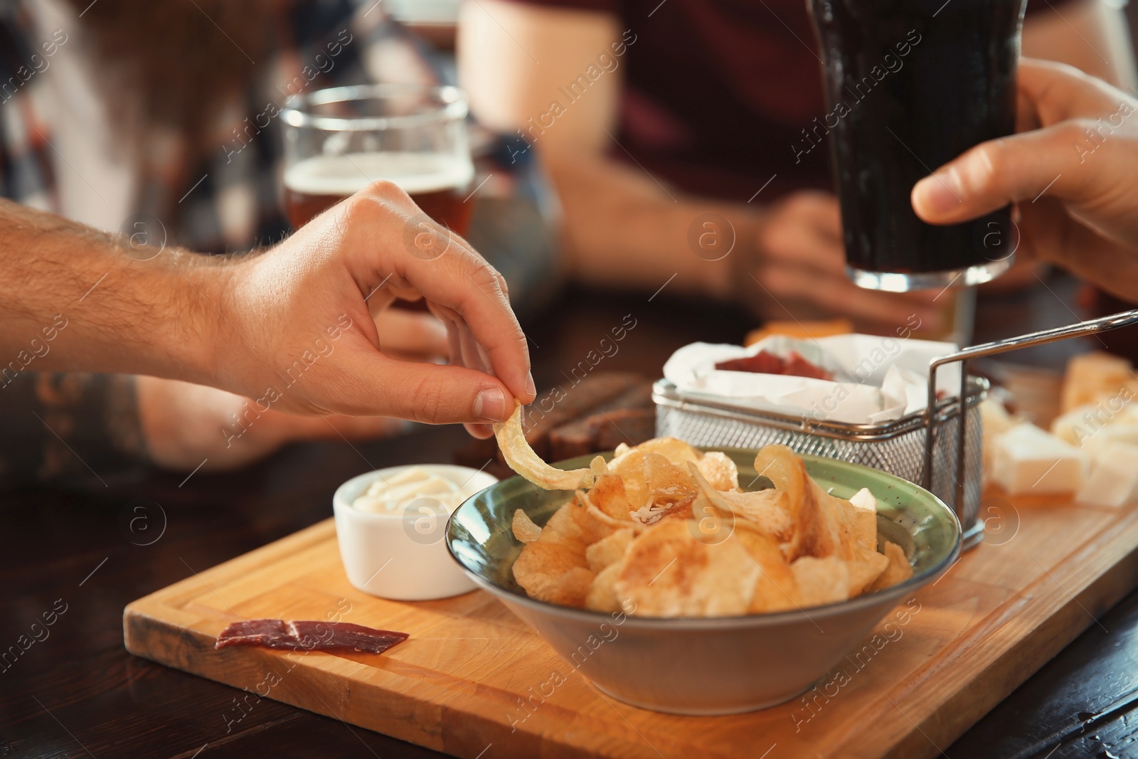 Photo of Friends drinking beer and eating snacks at table in pub