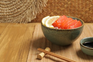Photo of Delicious salmon sashimi served with funchosa, lemon and soy sauce on wooden table, closeup. Space for text
