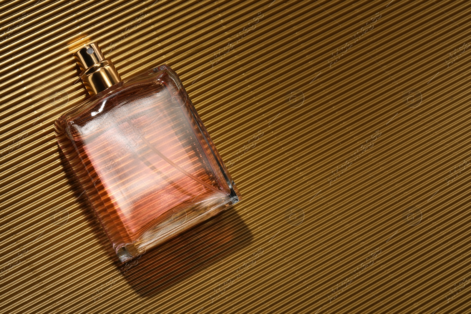 Photo of Luxury women's perfume. Sunlit glass bottle on golden surface, top view. Space for text