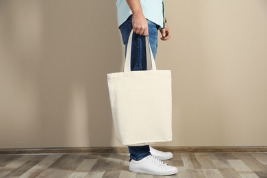 Young man holding textile bag against color wall, closeup. Mockup for design