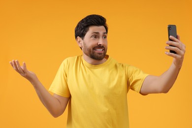 Puzzled man taking selfie with smartphone on yellow background