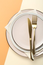 Ceramic plates, cutlery and napkin on color background, top view