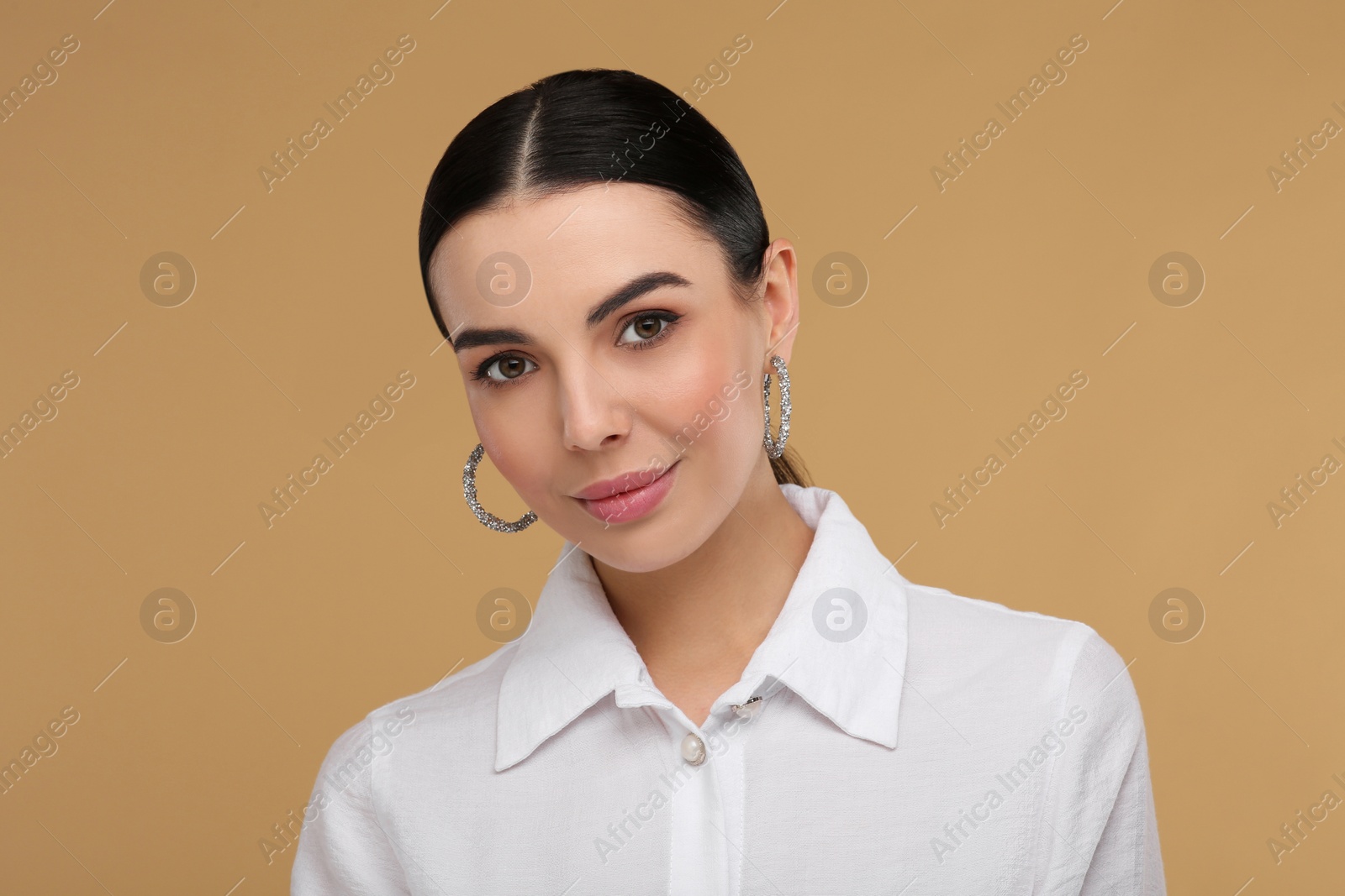 Photo of Beautiful young woman with elegant earrings on beige background