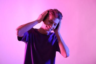 Photo of Young man with headphones on pink background in neon lights