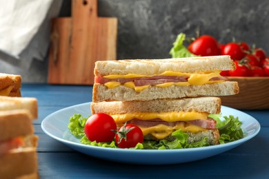 Photo of Tasty sandwiches with ham, melted cheese, lettuce and tomatoes on blue wooden table, closeup