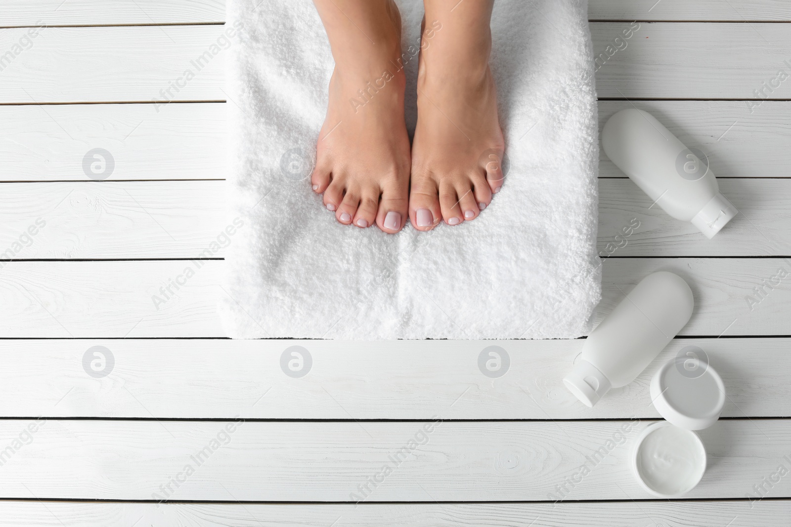 Photo of Top view of woman with beautiful feet, towel and cosmetic products on white wooden floor, space for text. Spa treatment