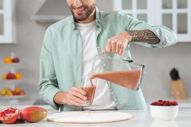 Photo of Man pouring tasty smoothie into glass at white marble table in kitchen, closeup