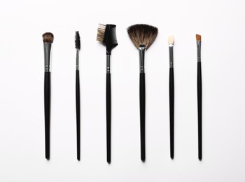 Different makeup brushes on white background, flat lay
