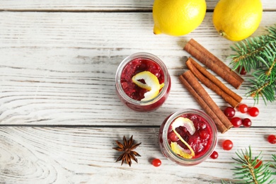 Photo of Flat lay composition with cranberry sauce in jars on white wooden background. Space for text