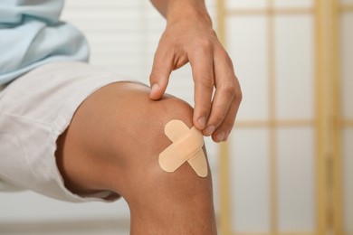 Photo of Man putting sticking plasters onto knee indoors, closeup