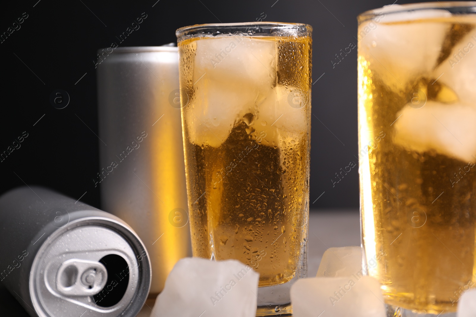 Photo of Tasty energy drink with ice cubes in glasses and aluminium cans on table, closeup