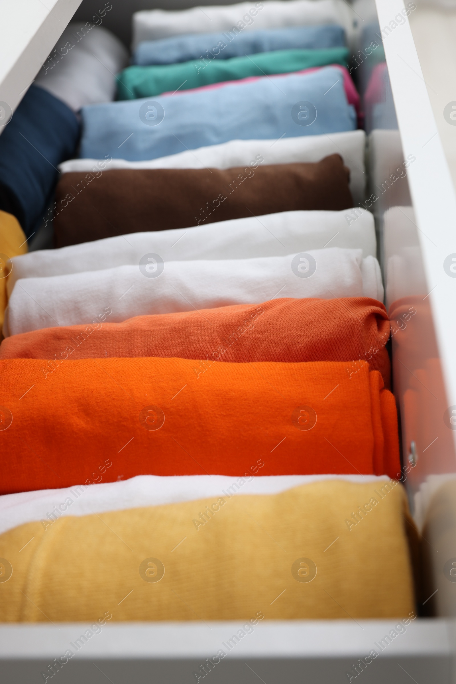 Photo of Different rolled shirts in drawer, closeup. Organizing clothes