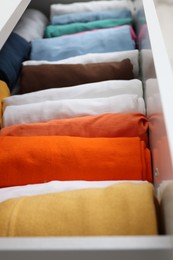 Different rolled shirts in drawer, closeup. Organizing clothes