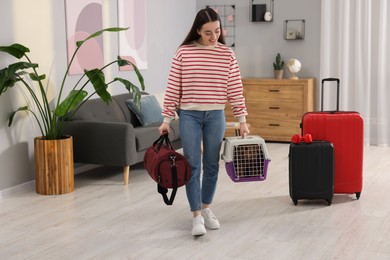 Photo of Travel with pet. Smiling woman holding carrier with dog and bag at home