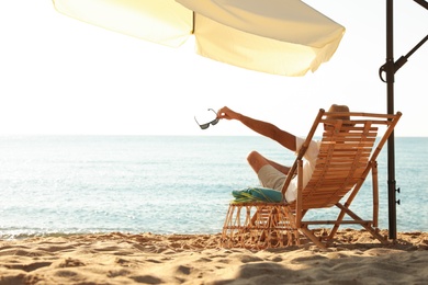 Man relaxing on deck chair at sandy beach. Summer vacation