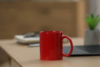 Photo of Red ceramic mug and laptop on wooden table at workplace