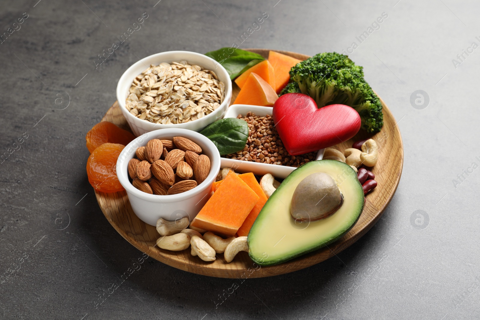 Photo of Wooden plate with heart-healthy products on grey background