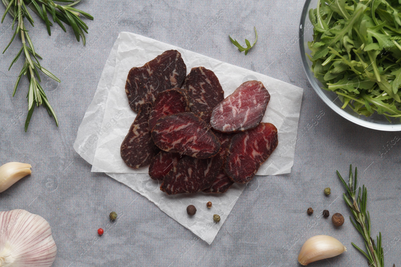 Photo of Slices of delicious beef jerky and spices on grey marble table, flat lay