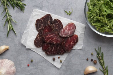 Slices of delicious beef jerky and spices on grey marble table, flat lay