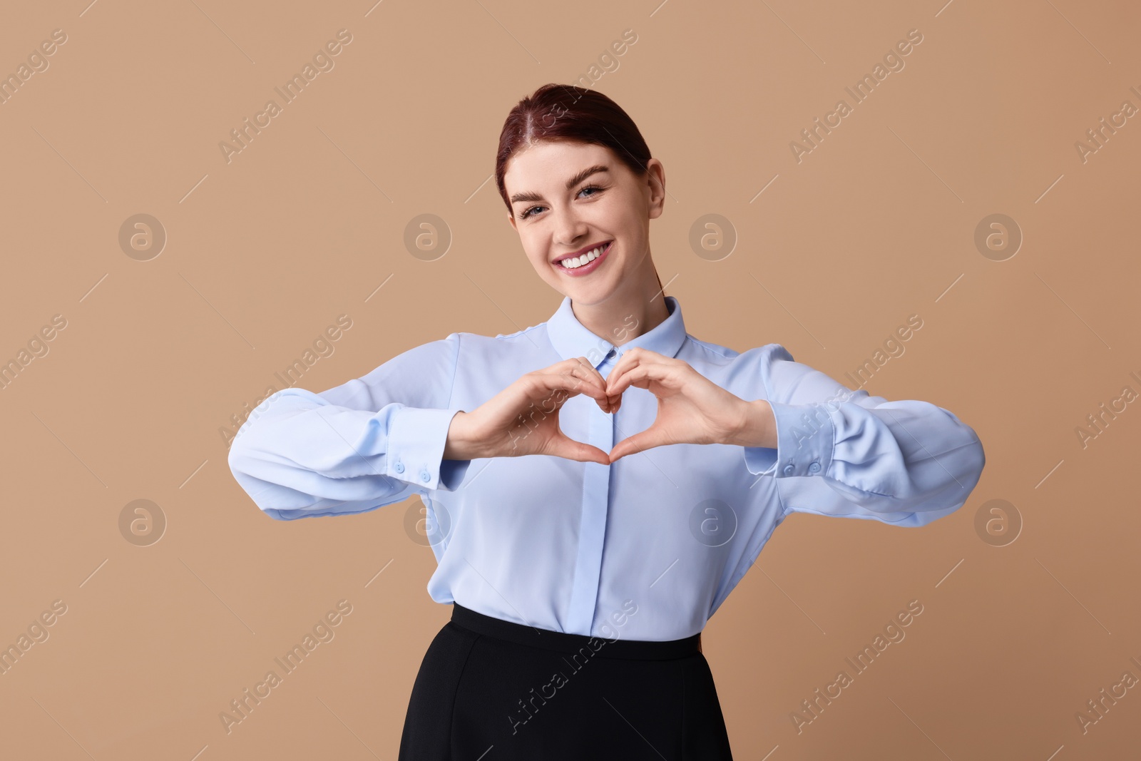 Photo of Happy young woman showing heart gesture with hands on beige background