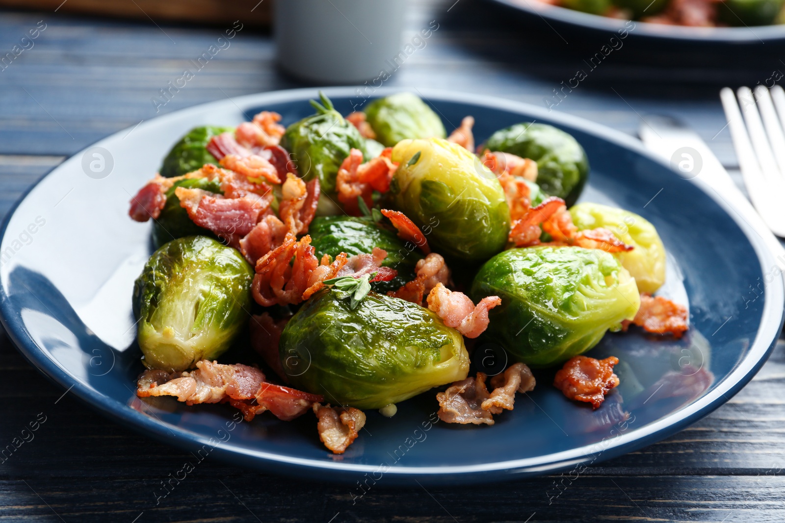 Photo of Tasty roasted Brussels sprouts with bacon on blue wooden table, closeup