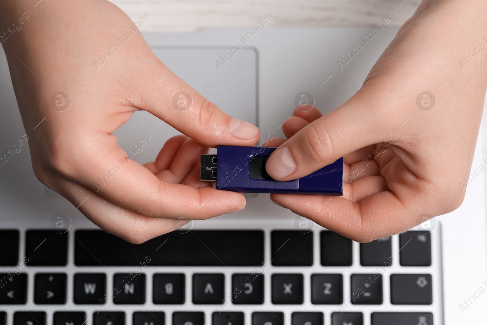 Photo of Woman holding usb flash drive at white wooden table, top view