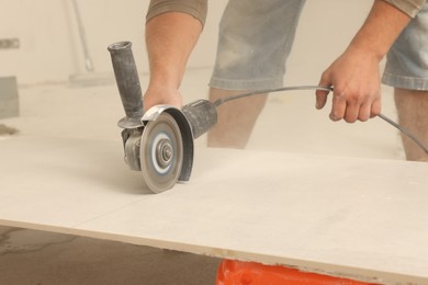 Photo of Worker cutting tiles with circular saw indoors, closeup