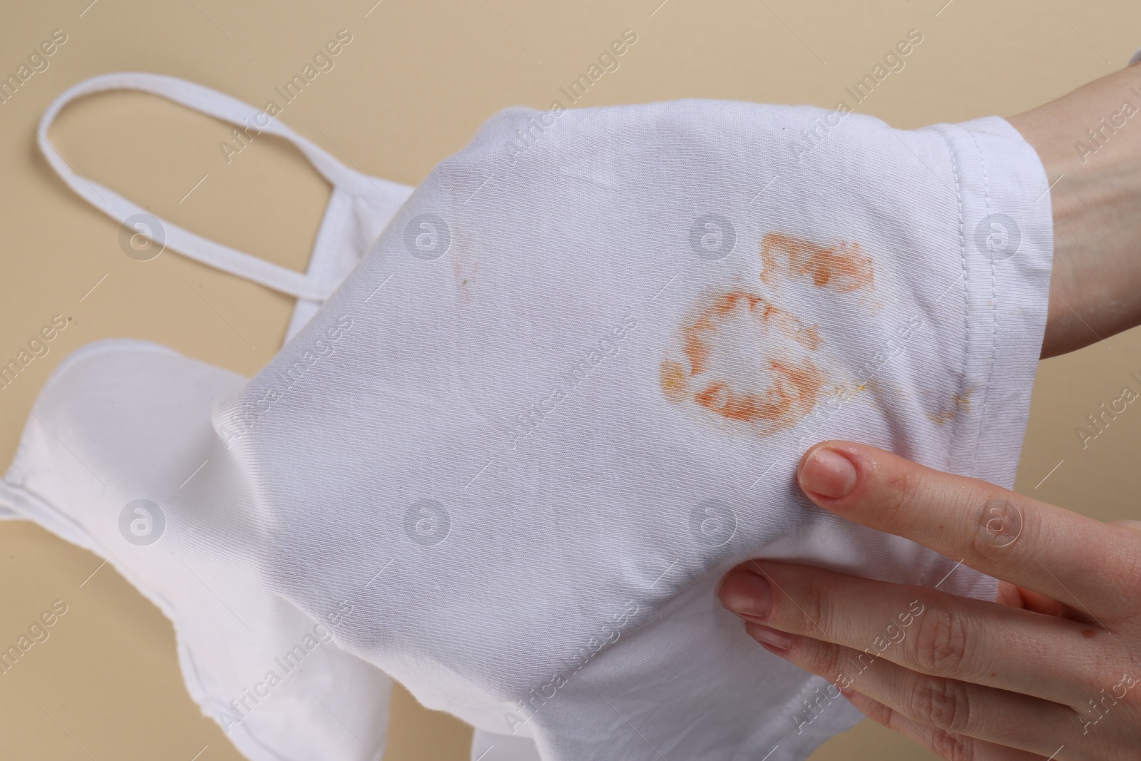 Photo of Woman holding white shirt with yellow stains on beige background, closeup