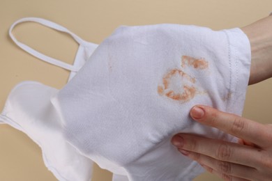 Woman holding white shirt with yellow stains on beige background, closeup