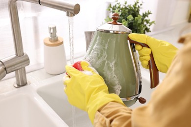Photo of Woman washing electric kettle with sponge at sink in kitchen, closeup