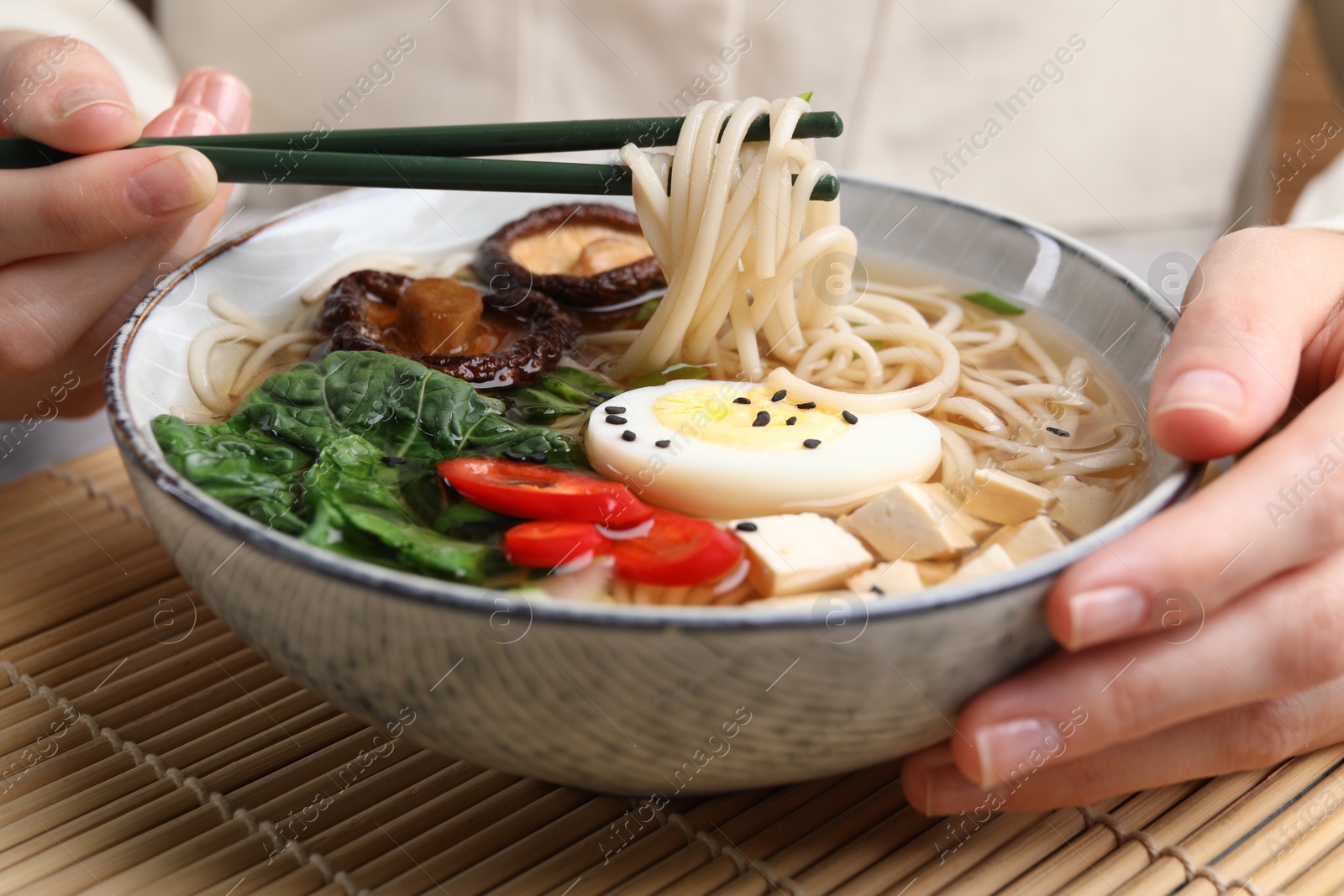 Photo of Woman eating delicious ramen with chopsticks at table, closeup. Noodle soup