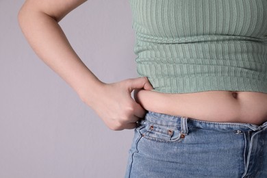 Photo of Woman wearing tight clothes on light grey background, closeup. Overweight problem