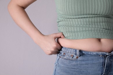 Woman wearing tight clothes on light grey background, closeup. Overweight problem