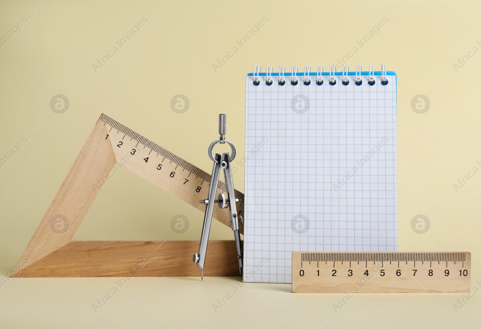 Photo of Triangle, notebook, protractor and compass on yellow background